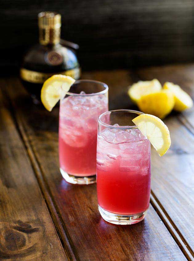 "Pink lemonade vodka cocktail on a table with lemons and bottle">